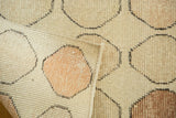 Playful apricot, blush, and coffee circles on faded beige Oushak pile, showing a secure edge.