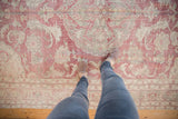 Looking down at the distressed, low-pile texture of a vintage Oushak in faded red and silver.