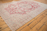 Angled view of the distressed Oushak's evenly worn pile and faded red floral medallion.