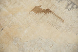 Distressed Oushak rug with faded brown motif on a light beige textured pile.
