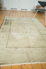 Corner of distressed vintage Oushak carpet showing pale beige and blush abrashes, checkered border.