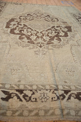 Low-pile texture and heavy abrashes on the medallion and beige field of a vintage Oushak carpet.