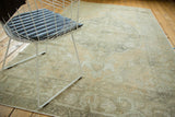 Angled view of a distressed vintage Oushak rug with faded beige, gray, and peach scrolling design.