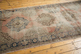 Distressed Oushak runner showing dusty rose field, muted splayed medallion, and navy palmette border.