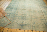 Distressed vintage Persian Meshed rug corner, showcasing faded blue, beige floral patterns.