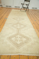 Distressed vintage Oushak runner's short pile, ivory and beige starburst medallion detail.