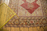 Distressed Oushak rug corner featuring pomegranate red, saffron yellow patterns, and worn pile.