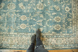 Textured distressed Oushak rug with faded blue-green and apricot floral patterns.