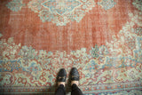 Feet on distressed Arak rug, showing worn rust field with powder blue floral motifs.