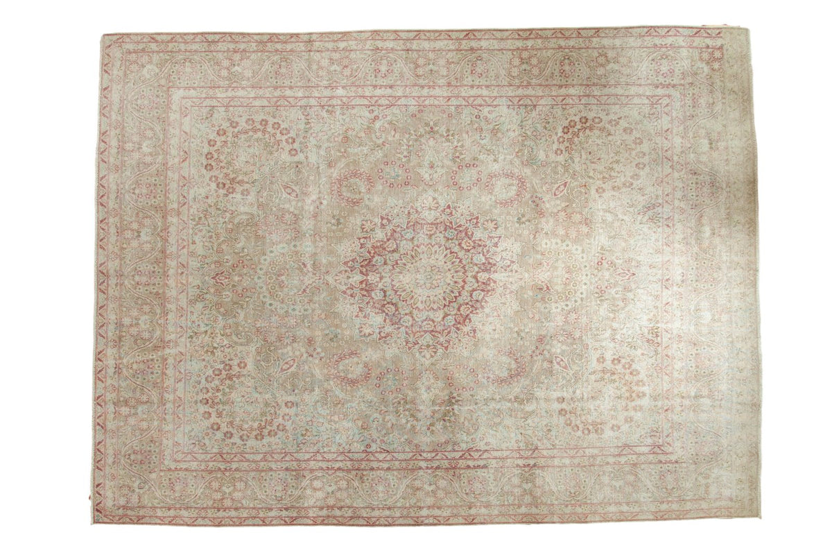 Distressed vintage Persian carpet with a raspberry red medallion on a sand-colored millefleur field.
