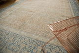 Distressed vintage Persian carpet with faded blush tones, light blue botanical patterns, and even wear.