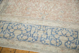 Distressed vintage carpet showing sky blue border with antique ivory vase and vine design.