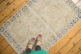 Distressed vintage Persian rug corner, highlighting worn beige field and a denim blue geometric border.