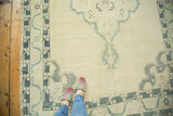 Distressed vintage Oushak carpet pile showing dusty green meandering vine border and cloud band spandrel.