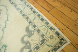 Distressed Oushak rug corner, showing pale field, muted green spandrel, and fringe.