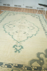 Distressed vintage Oushak rug showing pale field, dusty green medallion detail, and vine border.