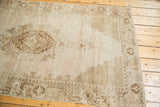 Distressed vintage Oushak rug corner, showing even wear and faded beige and brown motifs.