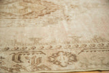 Faded beige and chocolate brown patterns with visible wear on a distressed Oushak rug.