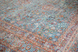 Intricate scrolling tendril and floral patterns on distressed sky blue Meshed rug corner.