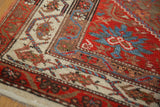 Corner view showing the ivory Serbend border, brick red field, and wear across the knot heads.