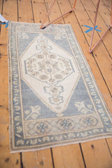 Close-up: distressed ivory Oushak rug, faded ink blue border, hexagonal floral medallion.