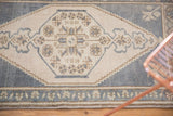 Distressed Oushak rug showing faded ink blue geometric motifs on soft ivory with border.