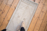 Distressed vintage Turkish Oushak rug in antique ivory, oxidized silver, with a person's feet.