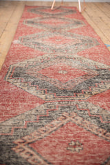 Worn cherry red Oushak runner with charcoal geometric patterns and exposed foundation.
