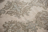 Distressed Oushak rug pile displaying densely ornamented floral patterns in sand beige and slate blue.