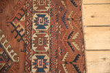 Antique Turkmen carpet showing geometric chestnut, navy, and beige patterns along the edge.