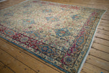 Distressed Kerman carpet corner revealing ivory, blue, and fuchsia Safavid-inspired floral motifs.