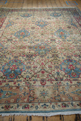 Ivory field and sky blue border details on a distressed Kerman carpet with rose floral motifs.