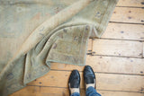 Distressed vintage Oushak rug displaying plush low pile, olive green, and intact side selvage.