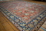 Safavid-inspired palmette and lotus design on brick red Tabriz carpet with navy border.