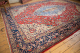 Distressed Laristan carpet corner: navy arabesque border, red floral field, with faux fringe.