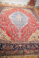 Vintage Distressed Laristan carpet with navy arabesque border, cherry red floral field, faux fringe.