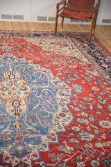 Distressed vintage Laristan carpet with low pile texture, cherry red field, and navy arabesque border.