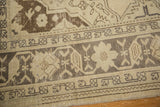 Distressed vintage Oushak rug detail: ivory field, charcoal geometric border, visible wear.