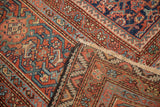 Antique Mahal carpet corner folded, revealing traditional herati motif in madder red, indigo, and ivory fringe.