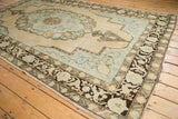 Distressed Oushak carpet corner, soft peach field, pale blue scalloped design, dark brown border.
