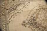 Distressed Oushak carpet with ivory field, brown scalloped medallion, and plant motifs.