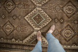 Repeating geometric medallions and hook motifs on vintage Serab rug in brown, ivory, and blue.