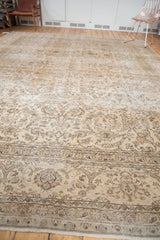 Distressed Sivas carpet featuring muted beige field, brown vinery, palmettes, and floral border.