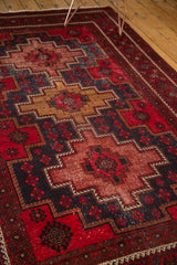 Vintage Belouch carpet with geometric red, gold, and navy medallion, featuring floral field and etching.