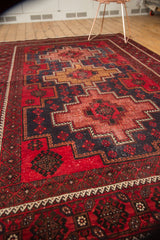 Belouch carpet corner detail with low pile, geometric patterns in cherry red, navy, and gold.