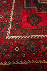 Cherry red vintage Belouch carpet with dark geometric motifs and cream zigzag border.