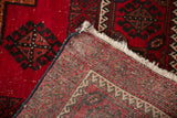 Belouch carpet corner folded to reveal tight hand-knotted foundation, cream fringe, and red geometric pattern.