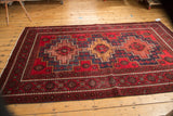 Geometric patterns and detailed borders of the Belouch carpet in cherry red, navy, and gold.
