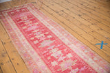 Distressed pink vintage Oushak runner, featuring floral effigies and curvilinear vine border.