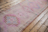 Distressed Oushak runner showing low pile, faded pink, blue, beige diamond border.